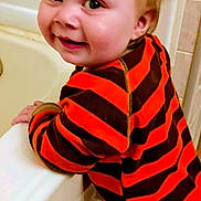 William is registered to the contest to win money with this photo: toddler, child, bathtub, bathroom, red_hair, striped_clothing, orange, brown, smile, face, person, young_child, cute, indoor, leaning, happy, clothing, hand, head, wall