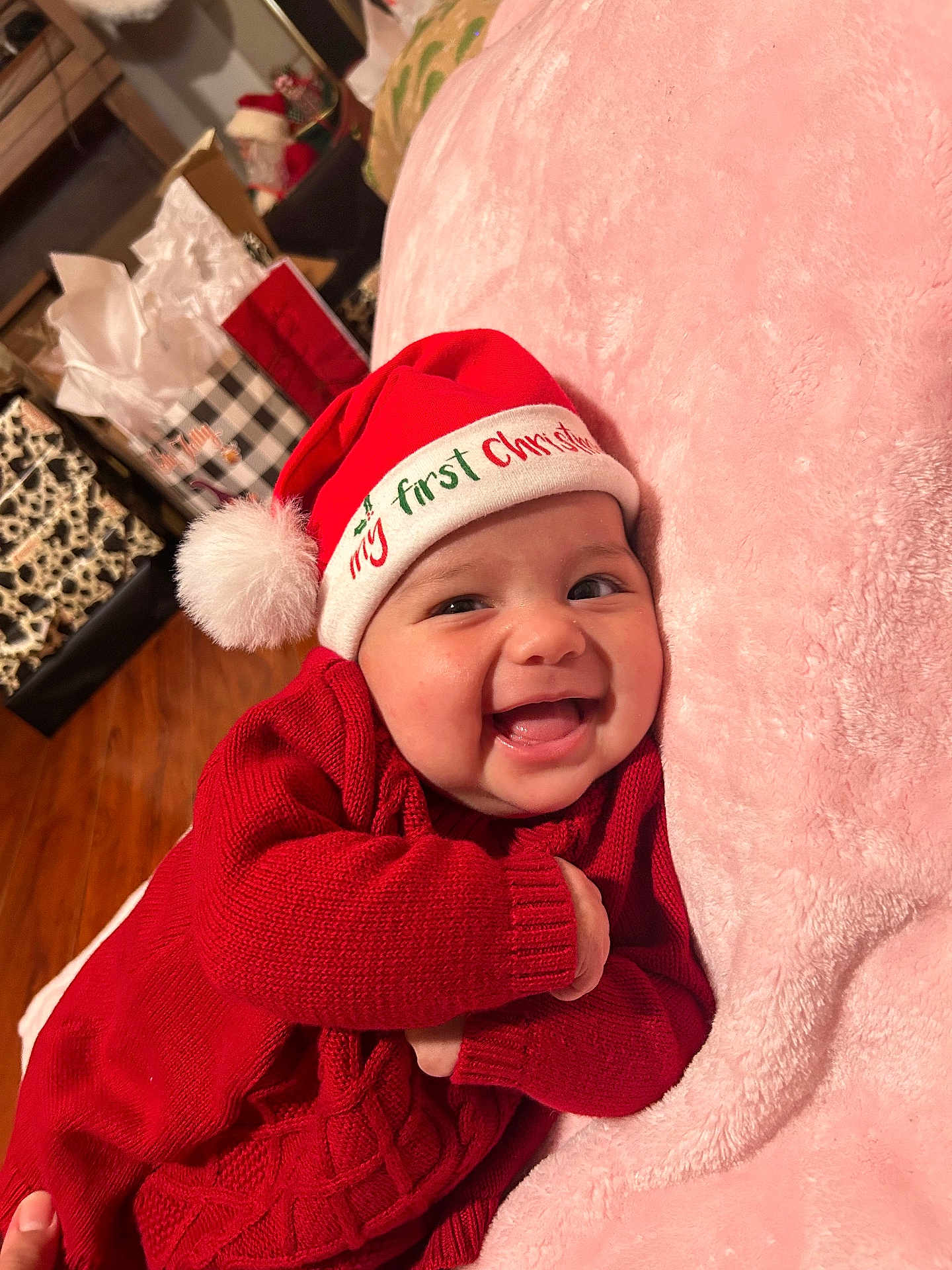 Kassandra is registered to the contest to win money with this photo: baby, smiling, red_sweater, santa_hat, christmas, holiday, infant, blanket, pink, happy, face, indoors, wooden_floor, gift_bags, festive, cozy, cute, child, portrait, celebration