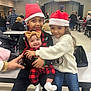 child, baby, santa_hat, holiday_clothing, smile, group, hug, indoor, event, table, bench, jeans, sweater, headwear, people, celebration, festive, community, family, joy