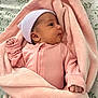 newborn, baby, infant, pink_blanket, pink_clothing, hat, striped_hat, wrapped, bed_sheet, leaf_pattern, curious, side_view, small_hand, cozy, soft_texture, fabric, sleepwear, cute, face, portrait