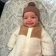 Kassandra joined the competition — help win amazing prizes! baby, smiling, infant, hat, pom_pom, cozy_clothing, fluffy, crib, mesh, leaf_pattern, blanket, cute, child, indoors, portrait, warm_clothing, lying_down, happy, face, person