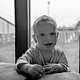 baby, black_and_white, blurred_background, child, couch, cozy, curious, cute, expression, face, hands, indoor, monochrome, person, portrait, smiling, soft_focus, toddler, window, young