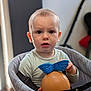 Andréas participe au concours pour gagner de l'argent avec cette photo : baby, background_blur, blue_bow, casual_clothing, child, closeup, curious, expression, face, high_chair, holding, home, indoor, light, person, seat, toddler, toy, wooden_table, young_child