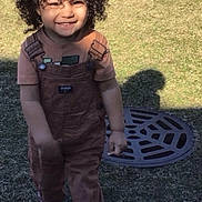 Luca joined the competition — help win amazing prizes! brick_building, casual_clothing, child, curly_hair, daytime, footwear, grass, happy, outdoor, overalls, person, play, shadow, smiling, sneakers, sunlight, toddler, walking, young_child