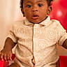 baby, child, portrait, sitting, red_chair, curly_hair, smiling, wide_eyed, indoors, fashion, shirt, shoes, infant, dark_skin, red_background, photography, close_up, seated, family_photo, cute