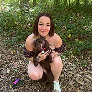 Shiva a rejoint le concours — aidez-le/la à gagner de superbes lots ! woman, puppy, dog, forest, trees, leaves, nature, outdoor, cute, smiling, tattoo, casual_clothing, short_hair, brown_dog, sneakers, sunlight, greenery, crouching, pet, happy