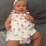 Ada-Violet is registered to the contest to win money with this photo: baby, child, smiling, dress, headband, cherry_pattern, infant, cute, happy, lying_down, bed, fabric, skin, hand, foot, indoors, person, apparel, headwear, portrait
