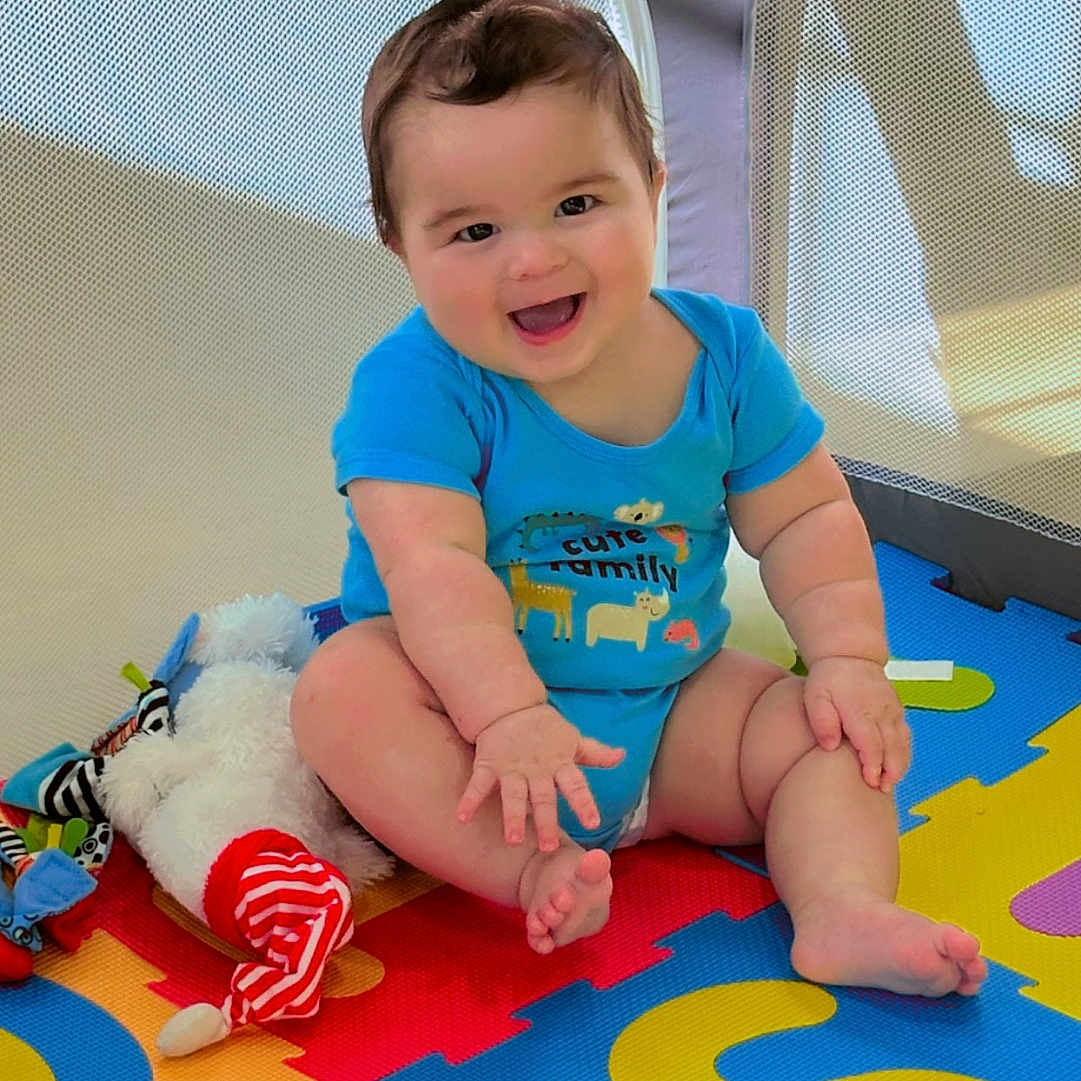 Kyliam is registered to the contest to win money with this photo: baby, blue_shirt, bright, cheerful, child, colorful, cute, floor, foam_mat, happy, indoors, infant, playpen, playtime, plush_toy, sitting, smiling, soft_toy, toys, young_child