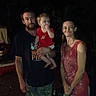 barefoot, beard, camouflage_pants, casual_clothing, child, dark_background, family, holding, man, night, outdoor, people, person, portrait, red_shirt, short_hair, smiling, standing, toddler, woman