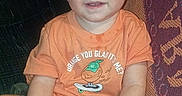 Rj is registered to the contest to win money with this photo: baby, blanket, camo_shorts, child, couch, cute, decor, feet, furniture, hands, happy, home, indoor, orange_tshirt, person, portrait, sitting, smiling, toddler, young_child