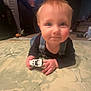 baby, child, toy_car, floor, indoor, living_room, television, person, play, crawling, denim_overalls, hand, face, blue_eyes, hair, furniture, carpet, home, light, cute