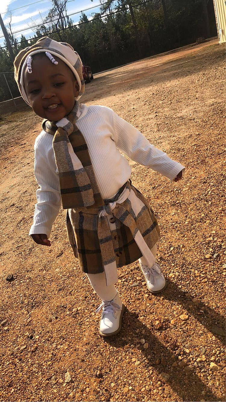 Erial is registered to the contest to win money with this photo: boot, child, fun, grass, grassland, happy, headwear, helmet, landscape, pattern, people_in_nature, person, personal_protective_equipment, plaid, play, shadow, sitting, sleeve, smile, soil