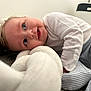 Logan is registered to the contest to win money with this photo: baby, child, infant, blue_eyes, white_shirt, striped_pants, soft_cushion, braided_cushion, lying_down, floor, indoor, curly_hair, happy, smiling, face, person, minimalistic_room, bright, cozy, cute