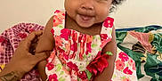 Maraya is registered to the contest to win money with this photo: baby, child, smiling, girl, dress, floral_pattern, curly_hair, sitting, indoor, hand, support, colorful, bedspread, happy, portrait, cute, infant, person, young_child, playful