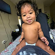 Maraya joined the competition — help win amazing prizes! baby, child, tongue_out, curly_hair, diaper, bracelet, indoor, bedroom, bed, person, smile, playful, candid, skin, cute, furniture, television, blanket, casual, relaxed
