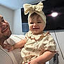 baby, child, man, smile, indoor, headband, bow, dress, holding, happy, portrait, television, furniture, person, family, expression, skin, hand, adult, cute