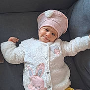 Valentyna a rejoint le concours — aidez-le/la à gagner de superbes lots ! baby, child, infant, couch, gray_background, knit_hat, pink_hat, white_jacket, bunny_patch, yellow_pants, smile, happy, cute, cozy, indoor, person, face, stretching, soft_texture, hand