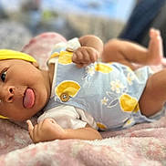 Amina is registered to the contest to win money with this photo: baby, infant, yellow_headband, blue_outfit, patterned_clothing, pink_blanket, tongue_out, lying_down, hands_up, legs_up, cute, soft_texture, indoors, closeup, child, newborn, playful, expression, face, skin