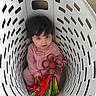 baby, basket, child, colorful, curly_hair, cute, floor, flower_toy, indoor, infant, laundry_basket, looking_up, person, pink_clothing, playful, portrait, sitting, soft_book, toy, white