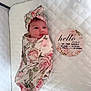 baby, birth_details, blanket, card, cute, face, floral_pattern, headband, indoors, infant, lying_down, newborn, peaceful, person, pink, portrait, quilted_bedding, soft, swaddle, white_background