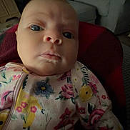 Eleanor joined the competition — help win amazing prizes! baby, infant, child, portrait, face, eyes, serious_expression, floral_clothing, onesie, seated, indoor, living_room, sofa, chair, cushion, home, close_up, photography, dim_lighting, colorful