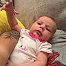 Eleanor joined the competition — help win amazing prizes! baby, infant, child, portrait, lying_down, indoor, couch, blanket, onesie, floral_pattern, pink_clothing, outstretched_hand, tattoo, adult_arm, cozy, face, eyes, photography, home, casual