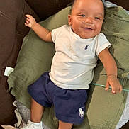 Javien joined the competition — help win amazing prizes! baby, child, smiling, couch, green_cushion, white_tshirt, navy_shorts, white_sneakers, nasal_cannula, happy, indoor, person, infant, clothing, footwear, relaxing, seated, cute, portrait, casual