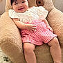 baby, child, smiling, infant, pink_clothing, headband, white_shoes, teddy_bear_chair, plush, cute, happy, indoors, soft_texture, seated, legs, hand, face, footwear, comfort, portrait