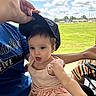 Serenity is registered to the contest to win money with this photo: toddler, child, baby, person, cap, dress, pink, hand, outdoor, sky, clouds, greenery, field, adult, glasses, blue_shirt, sitting, reaching, expression, sunny