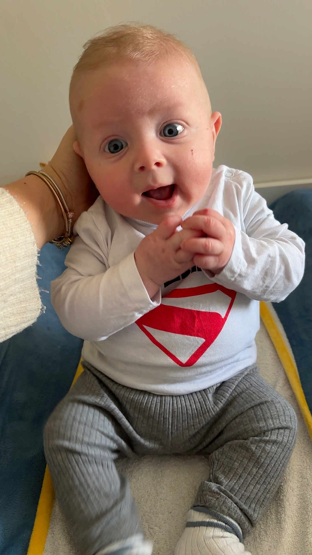 Malo participe au concours pour gagner de l'argent avec cette photo : baby, infant, child, blue_eyes, superhero_onesie, hands, clasping_hands, smile, open_mouth, adult_hand, bracelet, sitting, couch, blanket, socks, gray_pants, portrait, indoor, close_up, happy
