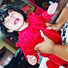 Cattaleya joined the competition — help win amazing prizes! child, toddler, curly_hair, red_outfit, being_held, adult, hands, indoor, portrait, face, closed_eyes, open_mouth, dramatic_expression, colorful_background, motion, family, infant, clothing, candid, photography