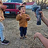 Elias is registered to the contest to win money with this photo: child, toddler, outdoor, pigeon, bird, animal, smiling, happy, standing, childhood, portrait, pickup_truck, vehicle, farmhouse, yard, gravel, trees, winter, adult, hand