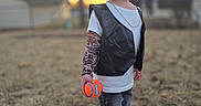 Elias is registered to the contest to win money with this photo: ball, child, golden_hour, grass, jeans, necklace, outdoor, portrait, shallow_depth_of_field, smiling, sneakers, standing, sunset, tattoo_sleeve, toddler, toy, trees, tshirt, vest, yard