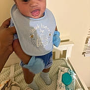 Hezekiah joined the competition — help win amazing prizes! baby, child, bib, blue_clothing, crib, baby_wipes, hand, indoor, person, toy, blanket, socks, face, expression, holding, home, infant, cute, playful, young