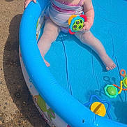 Lyla joined the competition — help win amazing prizes! toddler, child, inflatable_pool, toy, water, outdoor, sunny, red_hair, swimsuit, concrete, shoes, legs, summer, play, baby, sitting, colorful, blue, plastic, person