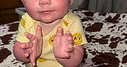Lyla is registered to the contest to win money with this photo: toddler, child, baby, clapping, yellow_shirt, sunflower_pattern, blue_eyes, red_hair, indoor, bedspread, patterned_bedspread, black_shorts, sitting, happy, cute, person, face, smiling, clothing, cozy