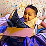 bib, blanket, cardboard_box, casual, child, clothing, colorful_wall, face, footwear, happy, indoor, jeans, paint_splatter, person, playful, portrait, room, shoes, toddler, toy_box