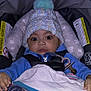 baby, blanket, blue_clothing, car_seat, child, cute, expression, eyes, face, footwear, hands, hat, indoor, infant, pacifier, pom_pom, safety_harness, seated, striped_pants, winter_wear