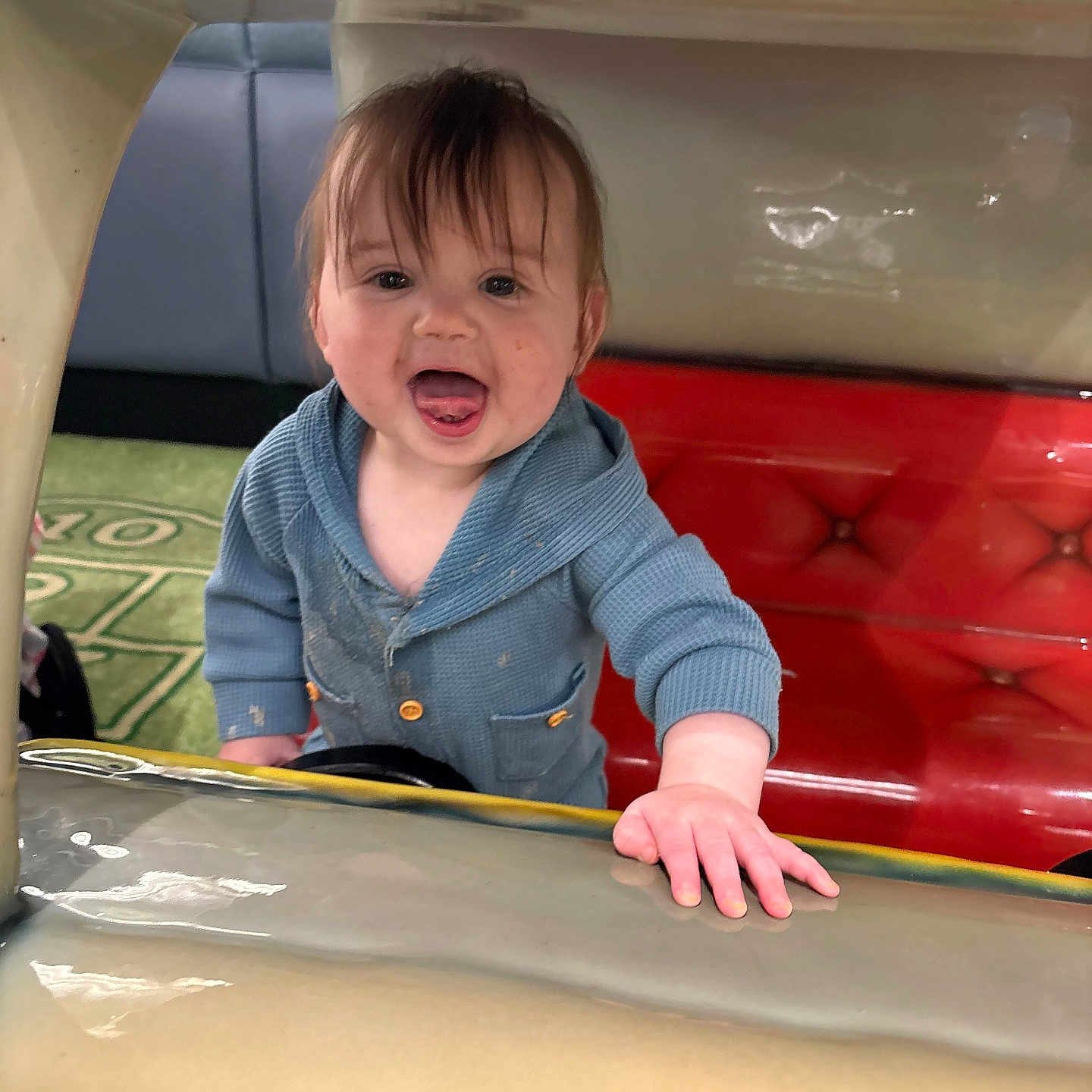 Osiris is registered to the contest to win money with this photo: toddler, child, smiling, blue_sweater, red_cushion, indoor, happy, face, hand, tongue_out, playful, person, young_child, clothing, curly_hair, floor_mat, colorful, cute, portrait, baby