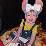 toddler, child, smiling, yellow_shirt, denim_overalls, mouse_ears, white_bow, book, blanket, indoor, happy, face, sitting, cute, playful, toy, colorful, portrait, young_child, cozy