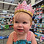 Maci joined the competition — help win amazing prizes! child, toddler, birthday_crown, shopping_cart, store, aisle, clothing, dress, blue, pink, face, person, cheeks, curly_hair, expression, indoor, retail, products, shelves, happy