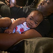 Armani is registered to the contest to win money with this photo: baby, adult, holding, phone, indoor, person, closeup, relaxing, casual, black_clothing, infant, portrait, family, candid, resting, comfort, interaction, face, hands, light