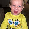 toddler, child, smiling, yellow_clothing, spongebob, indoor, happy, face, person, baby, long_sleeve, blue_eyes, short_hair, home, carpet, hand, toy, furniture, cheerful, portrait