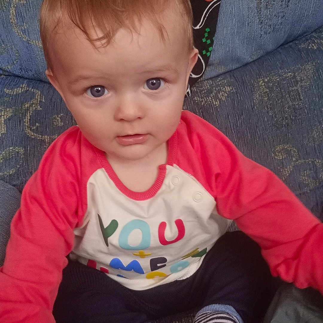 Vincent is registered to the contest to win money with this photo: baby, blue_eyes, casual, child, clothing, colorful_shirt, couch, curious, cute, hand, home, indoor, infant, person, plush, portrait, sitting, soft_lighting, striped_socks, young_child