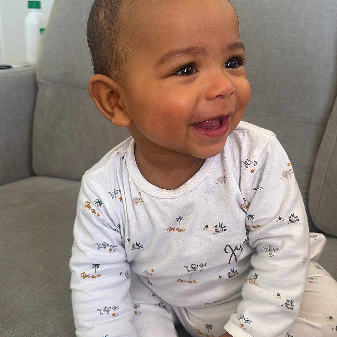 Khadim participe au concours pour gagner de l'argent avec cette photo : baby, child, couch, cute, eyes, feet, hair, hands, indoor, infant, laughing, living_room, looking_right, onesie, pajamas, portrait, sitting, smiling, sofa, toes