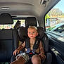 bare_chest, blonde_hair, blue_eyes, car_door, car_headrest, car_interior, car_seat, car_window, child, daylight, outdoor_scene, passenger, people_outside, safety_harness, seat, seatbelt, shorts, toddler, vehicle, window