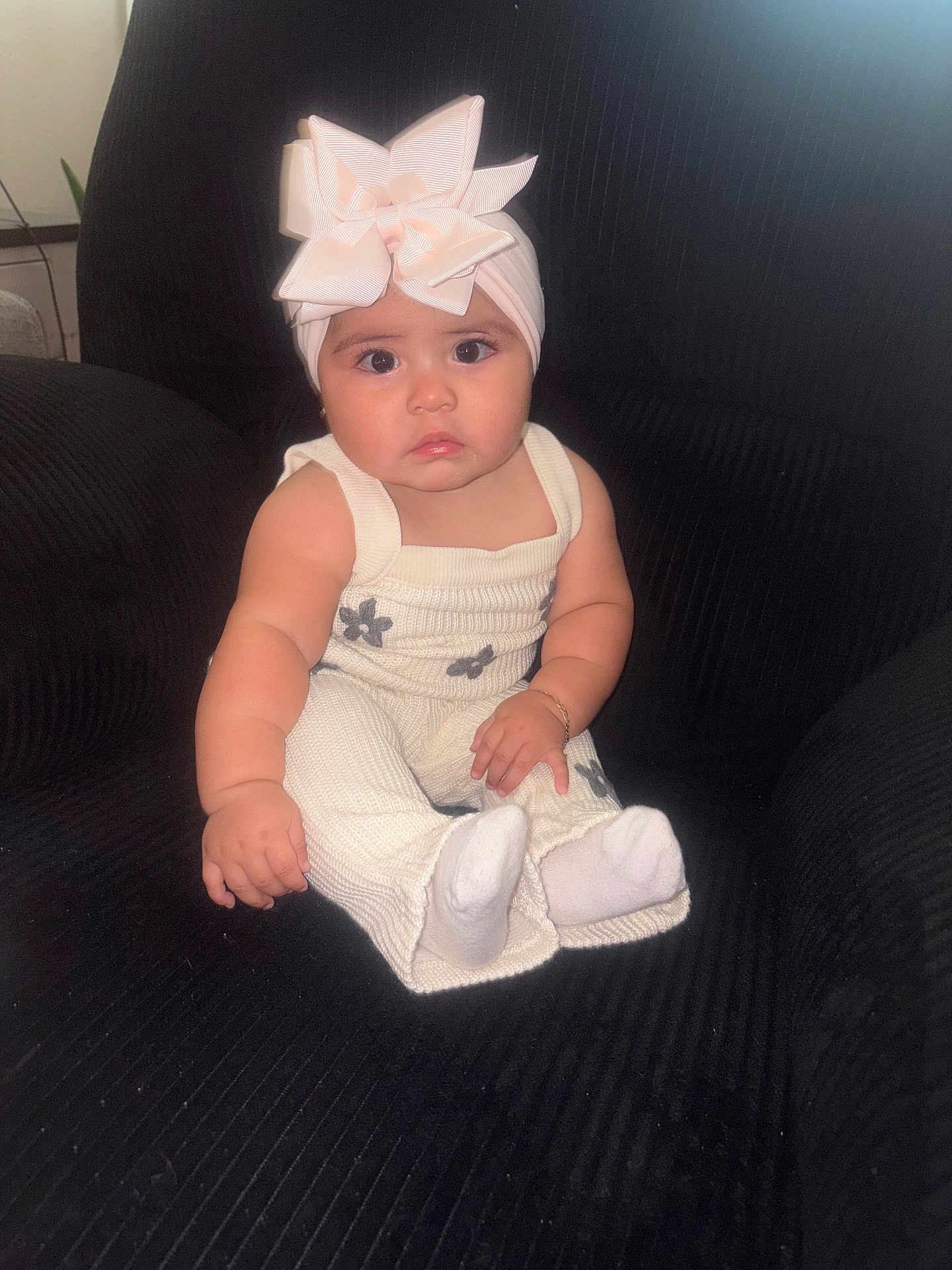 Hazel is registered to the contest to win money with this photo: baby, child, headband, bow, white_clothing, sitting, chair, black_chair, indoor, cute, portrait, infant, cute_expression, plush, cozy, small_bracelet, sock, curious, wide_eyes, pouting