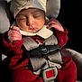 baby, sleeping, car_seat, red_clothing, white_hat, infant, safety_harness, close_up, cute, peaceful, child, newborn, portrait, indoors, soft_lighting, hands, face, cozy, resting, adorable