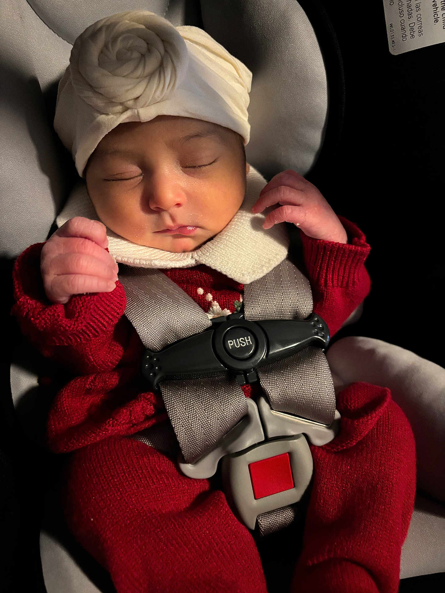 Ciara is registered to the contest to win money with this photo: baby, sleeping, car_seat, red_clothing, white_hat, infant, safety_harness, close_up, cute, peaceful, child, newborn, portrait, indoors, soft_lighting, hands, face, cozy, resting, adorable