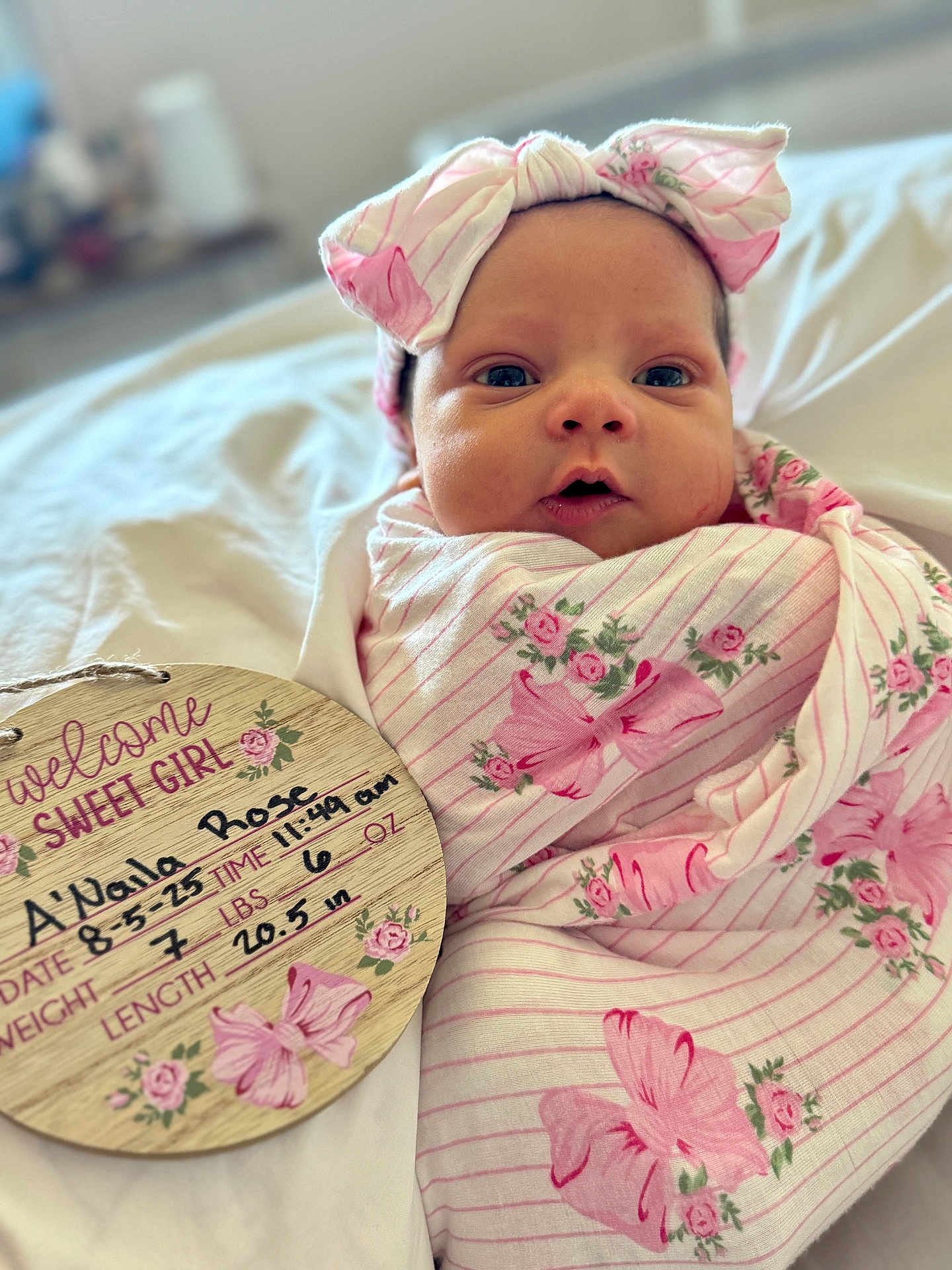 Anaila is registered to the contest to win money with this photo: baby, newborn, infant, blanket, headband, pink, floral, bed, plaque, birth_details, handwritten, cute, wrapped, portrait, sleeping_area, soft, closeup, person, child, indoors